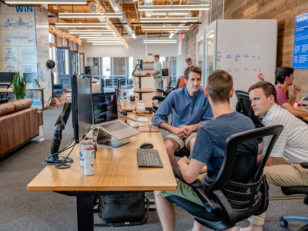 3 men chatting at a desk