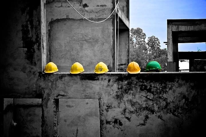 four coloured safety helmets resting on a wall at a construction site